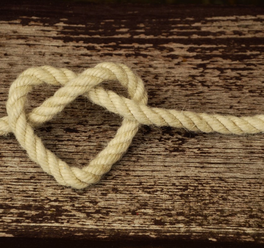 Seil in Herzform auf rustikalem Holztisch, Symbol für die Freude an Freiwilligenarbeit
