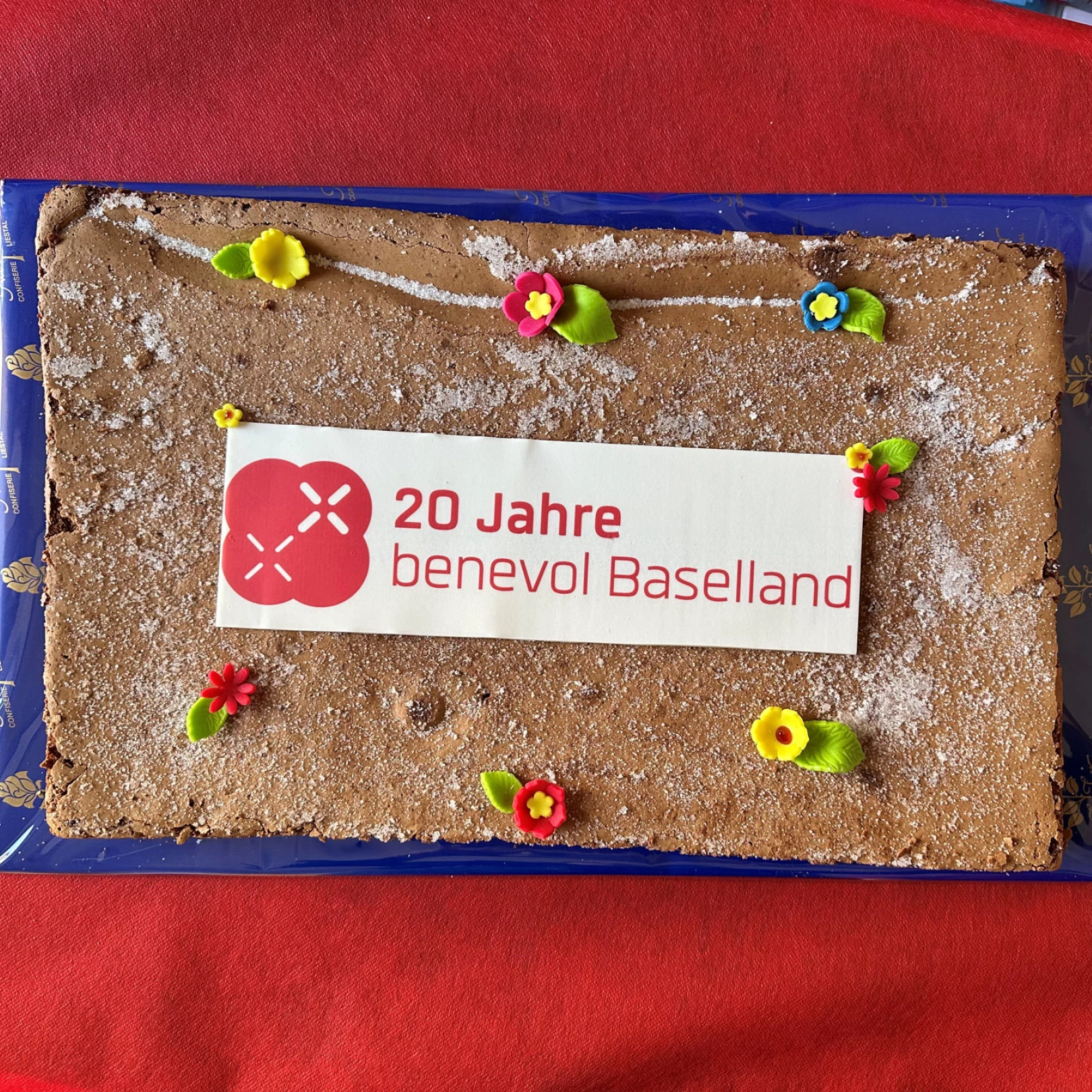 Jubiläumstorte mit Logo und Schriftzug «20 Jahre benevol Baselland» auf rotem Tischtuch